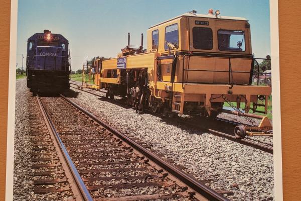 Promotional photo: An SD40-2 passes a continuous action tamper (CAT), used for compacting ballast under railroad ties. Conrail was the first U.S. railroad to use CAT equipment, which increases maintenance productivity.