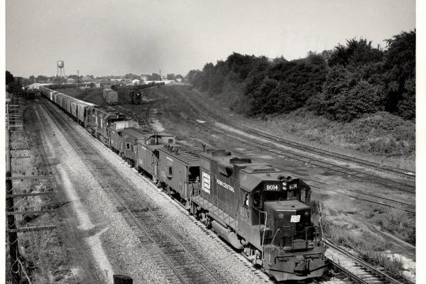 Photograph of GP38-2 8014, numerous cabooses and a westbound grain train at Orrville OH. 7/30/76