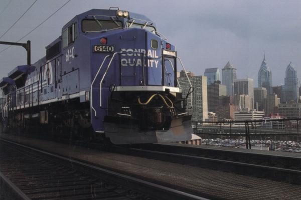 Wood Laminated Promotional photo: Philadelphia, Conrail's headquarters city, forms the backdrop for a GE C40-8 wide-cab locomotive on the 'high line,' just west of the downtown area.