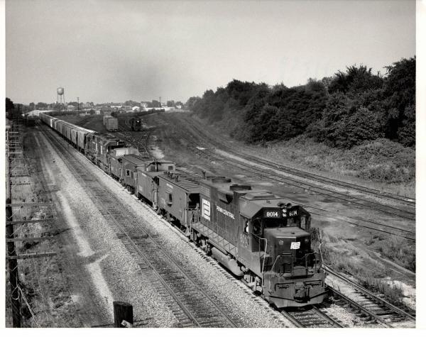 Photograph of GP38-2 8014, numerous cabooses and a westbound grain train at Orrville OH. 7/30/76